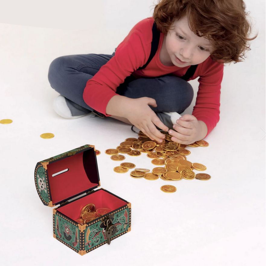 Child playing with a toy treasure chest and gold coins on a white floor.