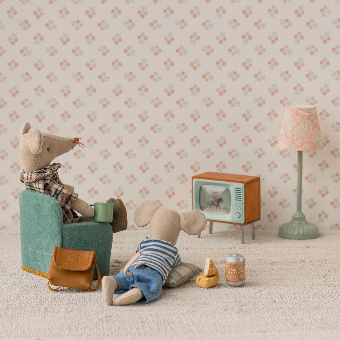 Miniature scene with toy mouse in a chair, child's legs, and vintage TV against a floral wallpaper background.