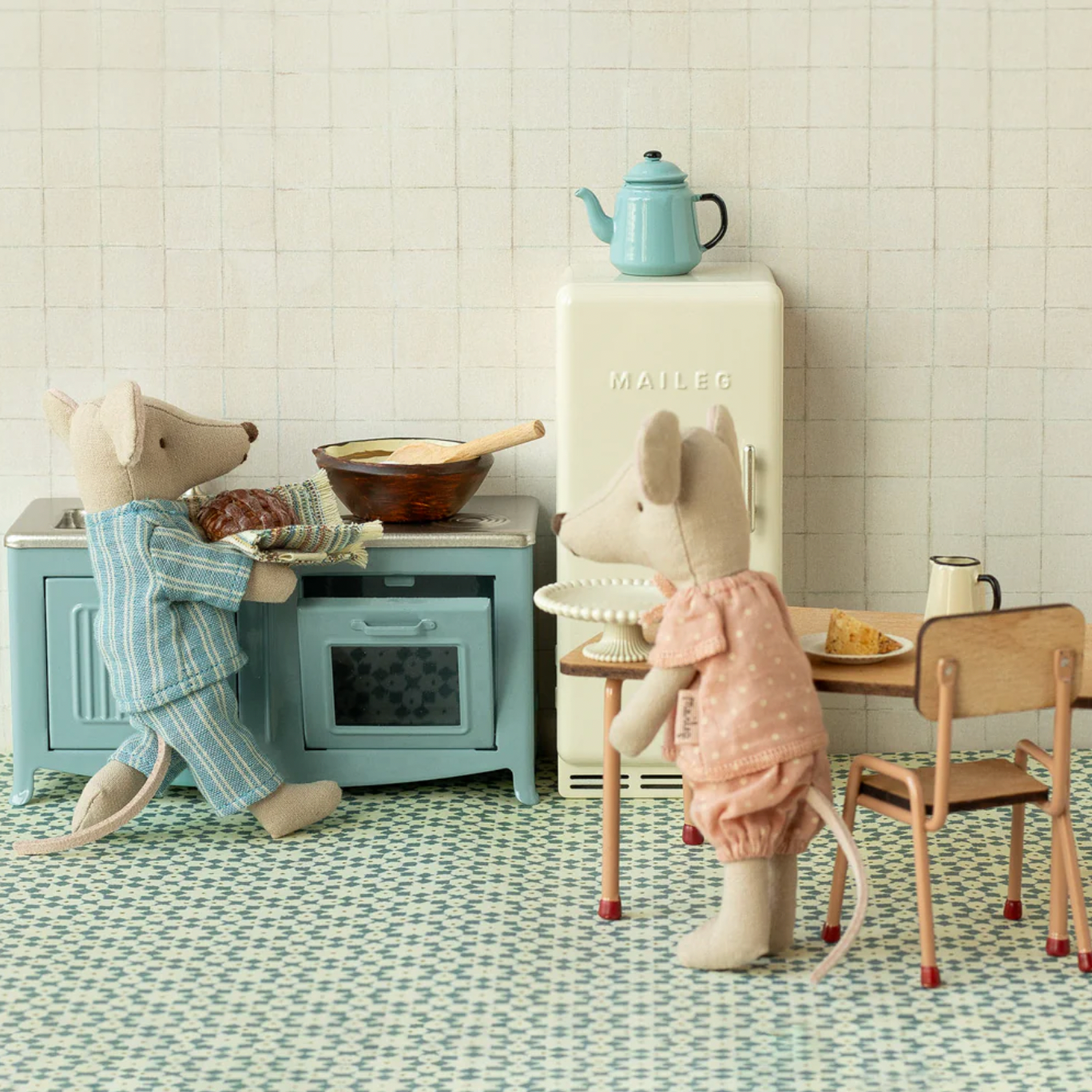 Miniature kitchen scene with toy figures and furniture on a patterned floor.