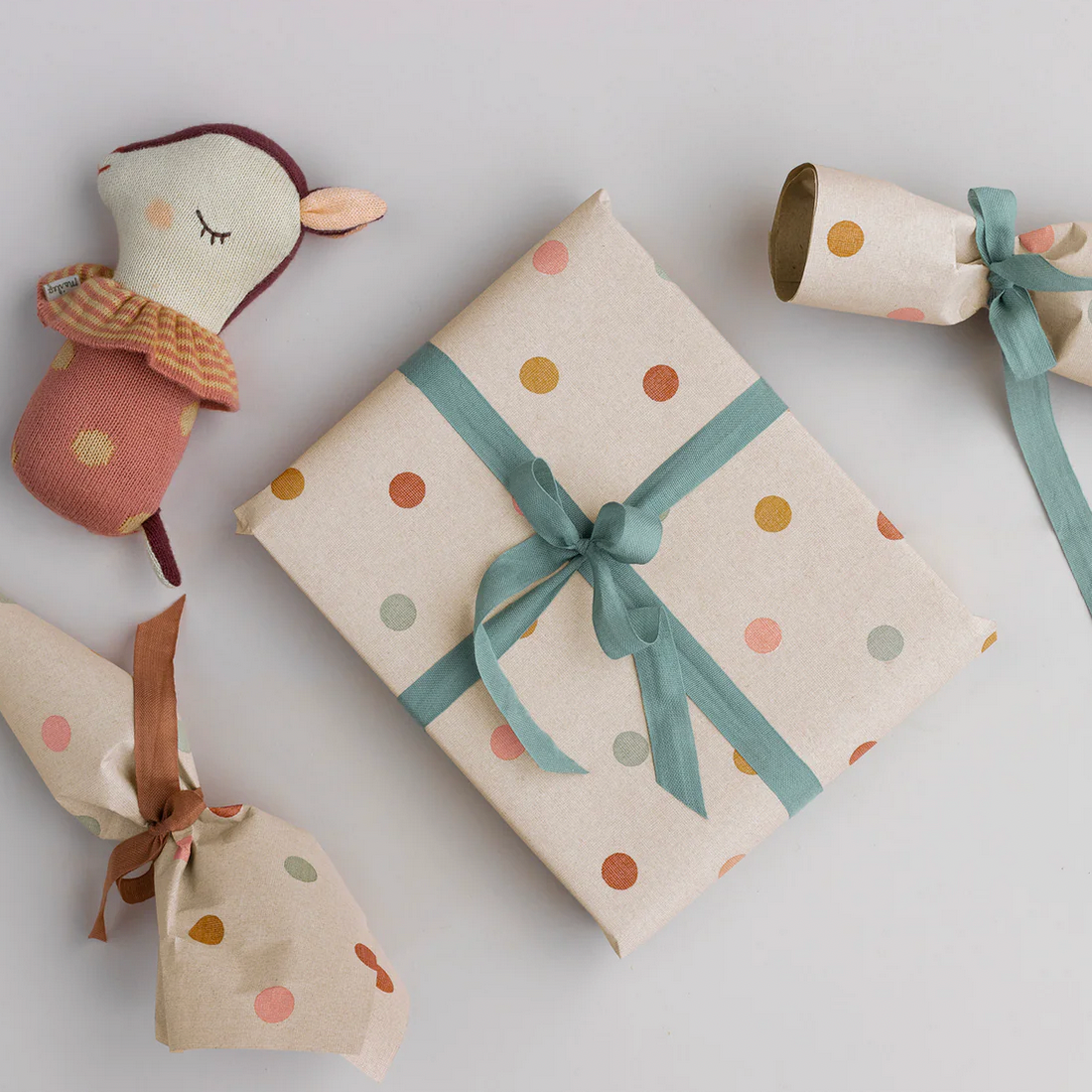 Gift wrapped in polka dot paper with ribbons, accompanied by a small plush toy on a light gray background.