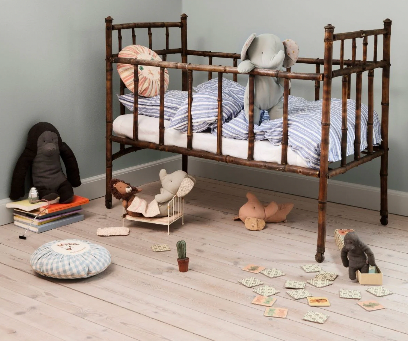 Wooden crib with striped bedding in a room with toys and books on the floor.