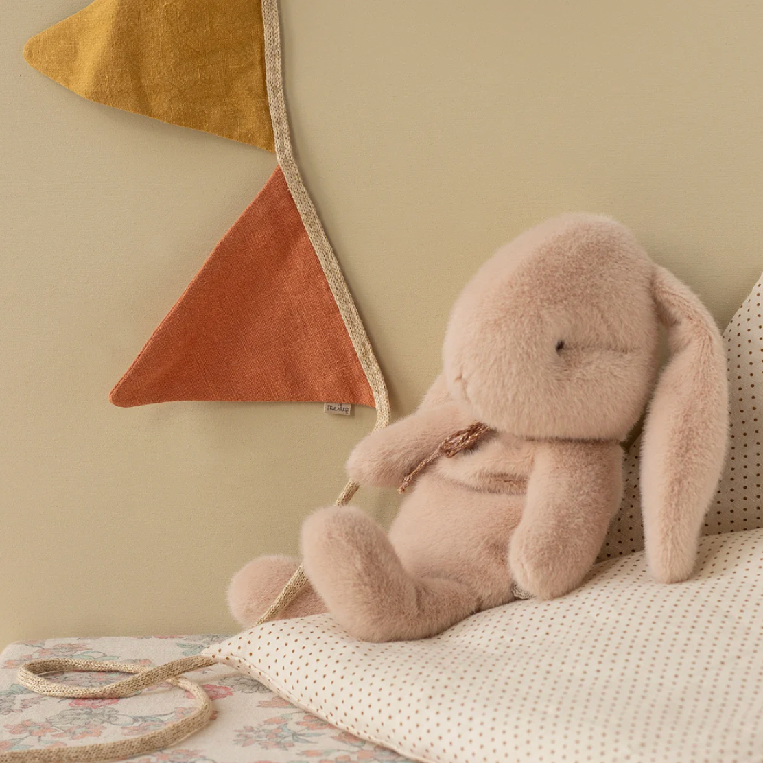 Plush bunny toy on a bed with decorative pillows and wall art in the background
