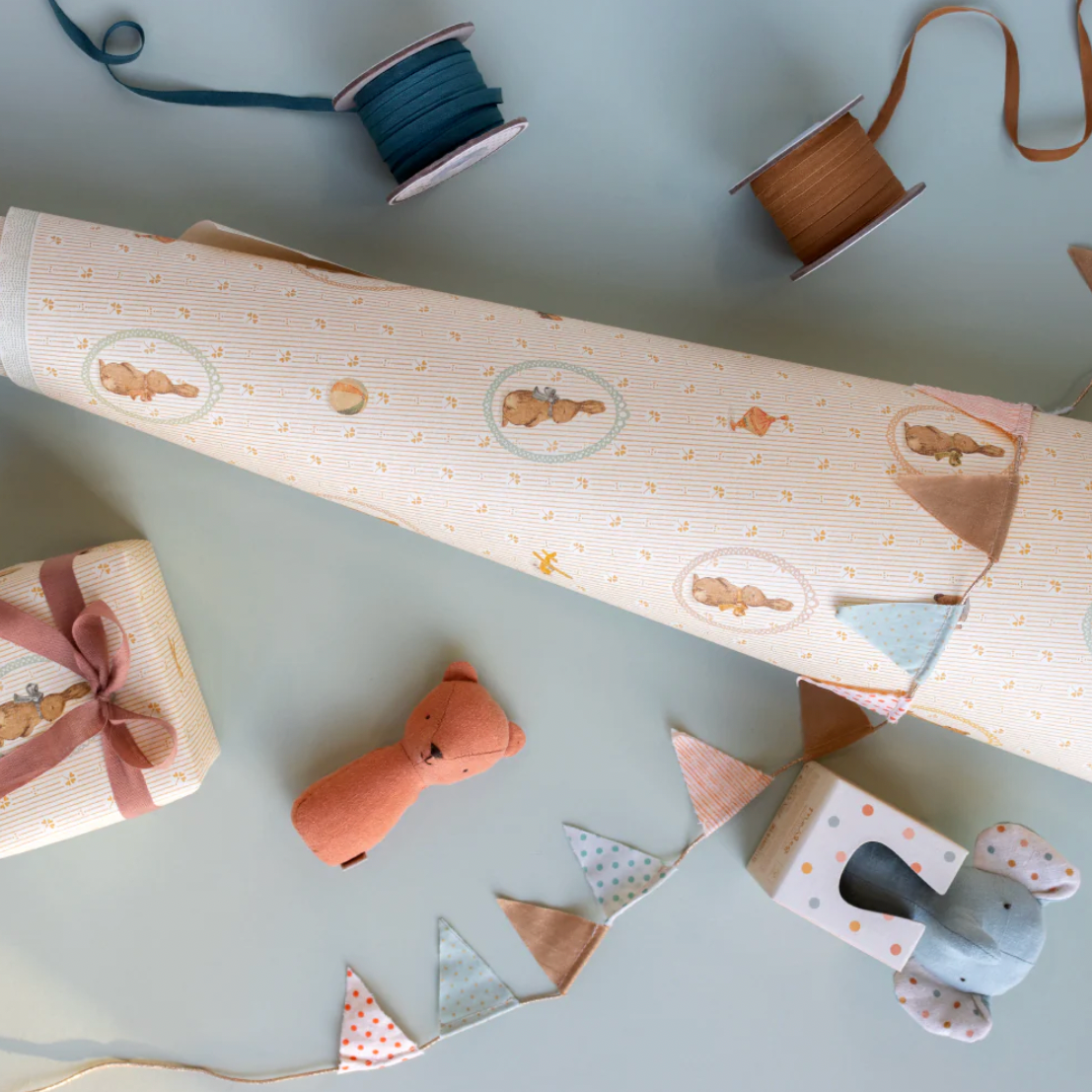 Gift wrap with teddy bear design on a light gray surface with ribbons and packaging tools.