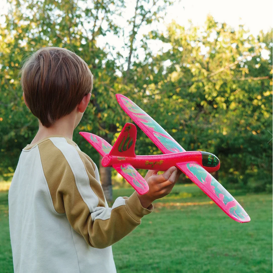 Child holding a pink and green toy airplane in a park