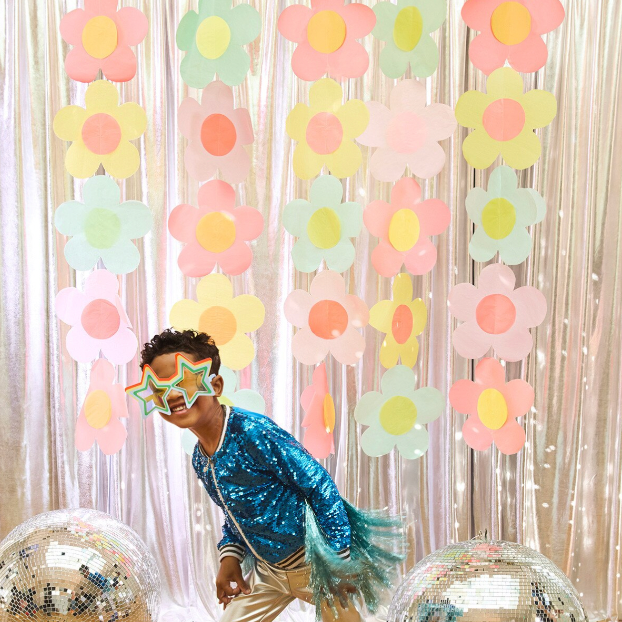 Person wearing a blue sequin outfit and star-shaped sunglasses in front of a floral backdrop.