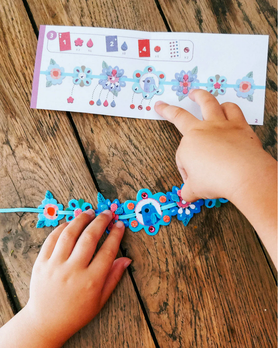 Child's hands working on a blue bracelet with floral designs on a wooden surface.
