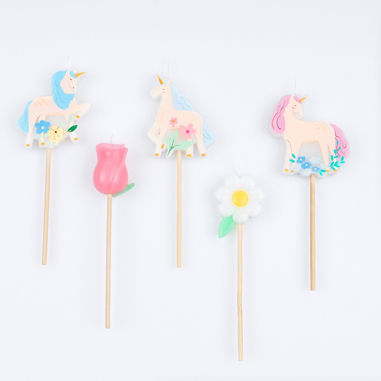 Unicorn-themed candles on sticks with pastel colors against a white background