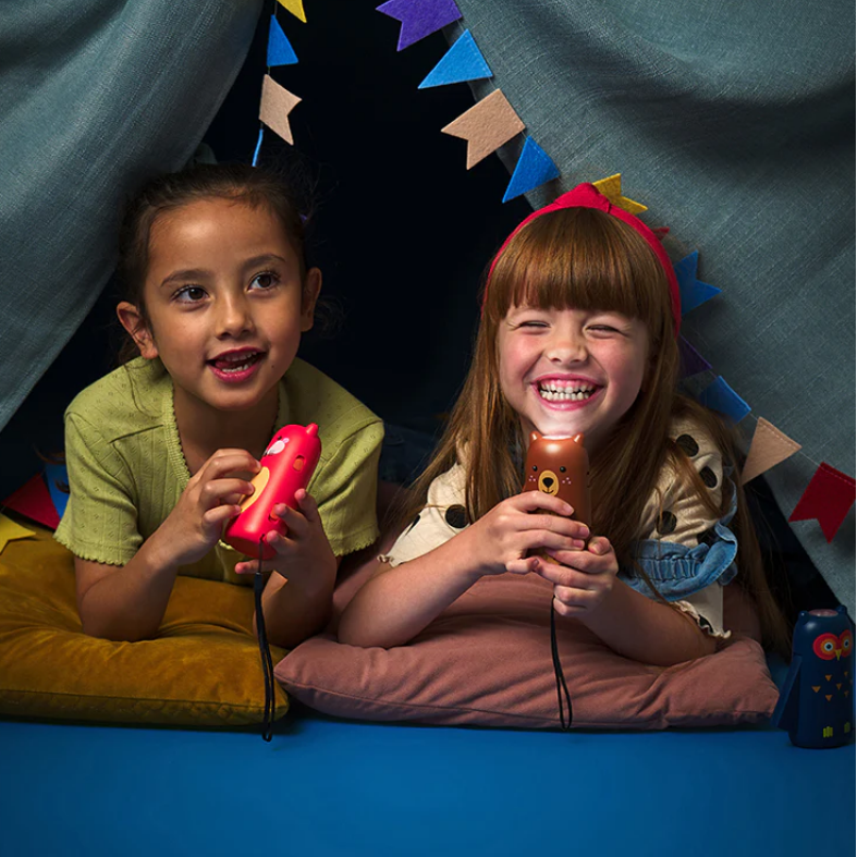 Two children playing with toy flashlights inside a homemade playhouse with colorful flags.