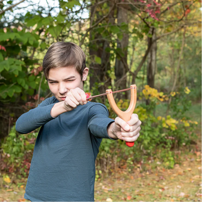 Child using a slingshot in a forest setting