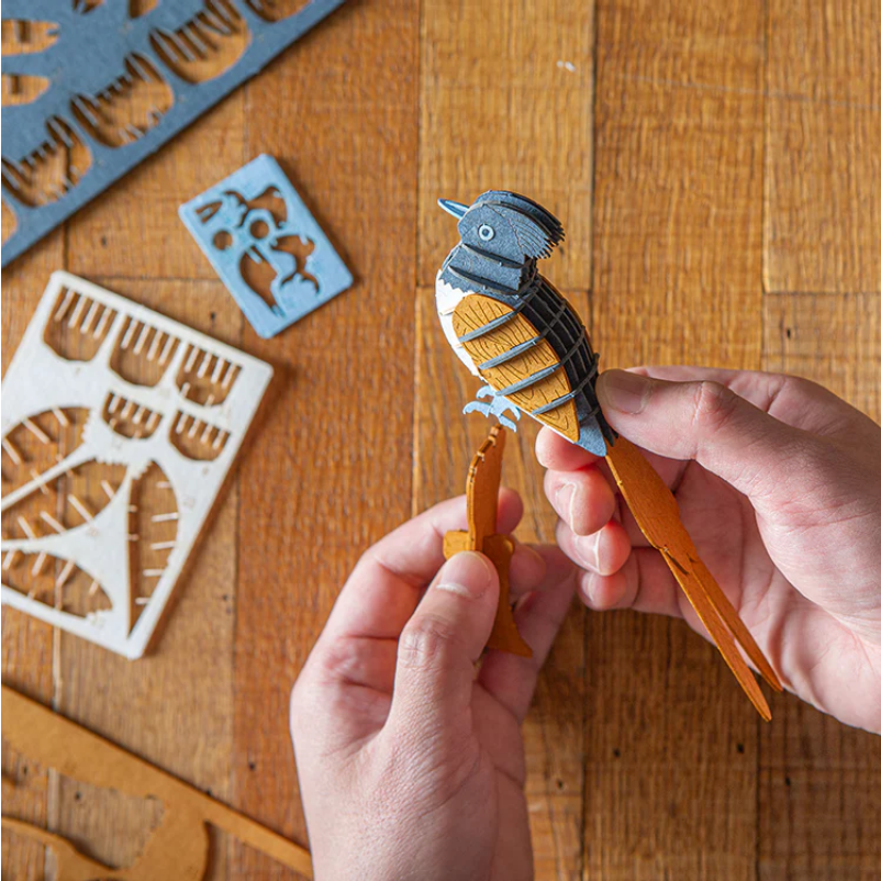 Hands holding a bird-shaped wooden tool with cut-out designs on a wooden surface