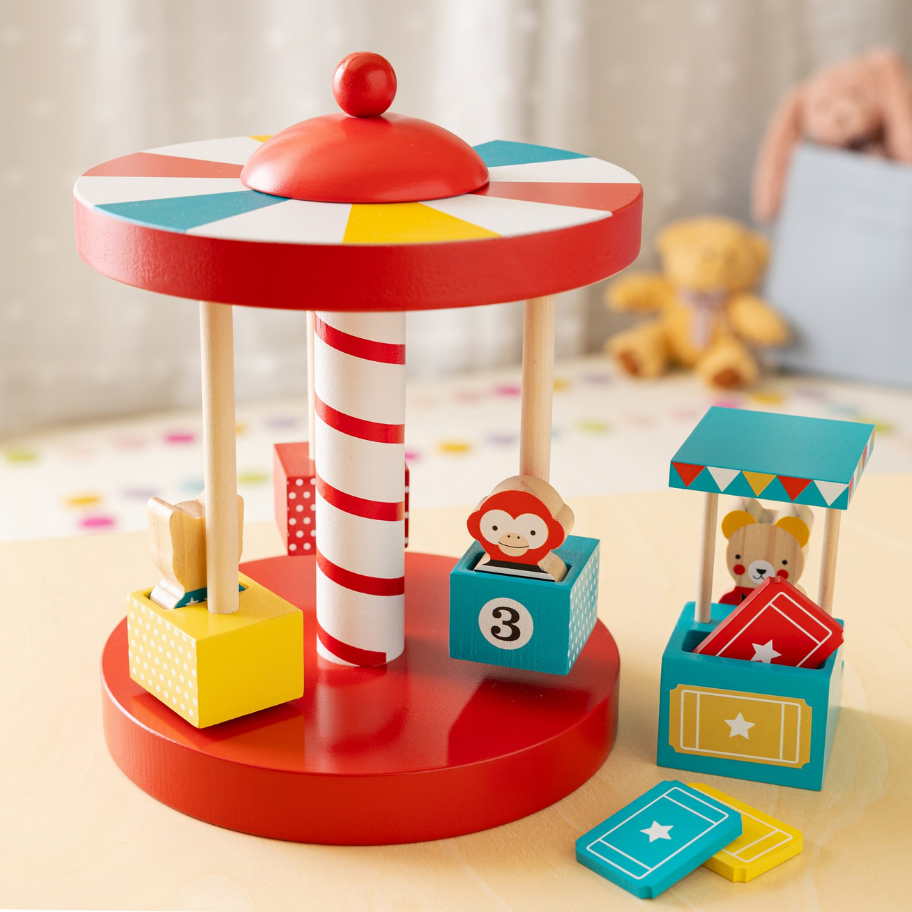 Colorful toy carousel with wooden figures on a light surface.
