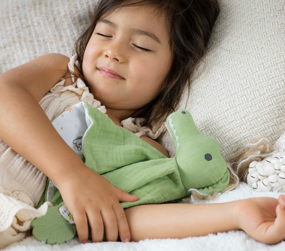 Child holding a green plush toy on a soft surface