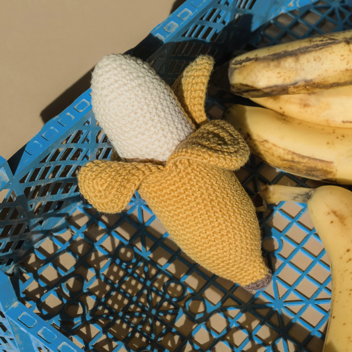 Knitted banana toy in a blue plastic crate with bananas