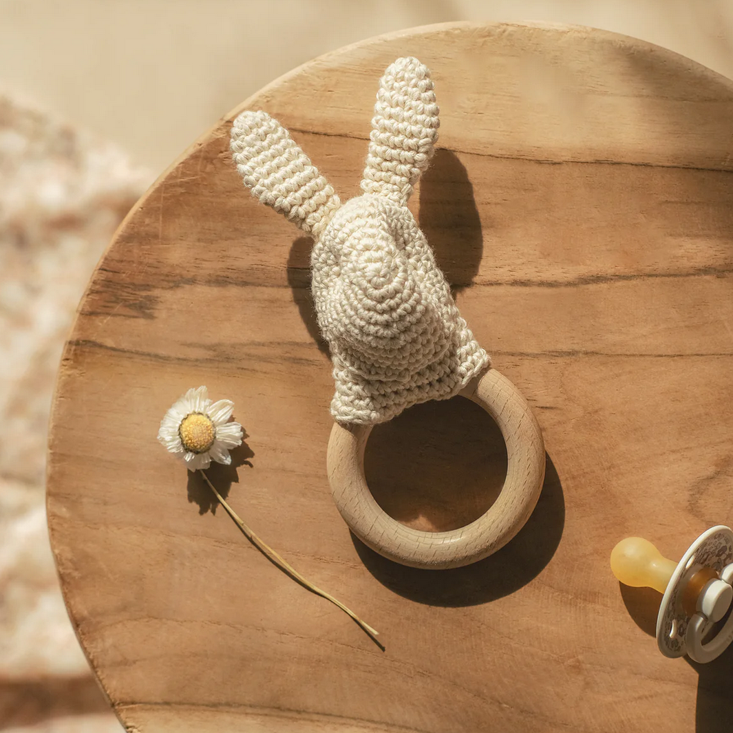 Crocheted bunny rattle on a wooden surface with a flower and pacifier.