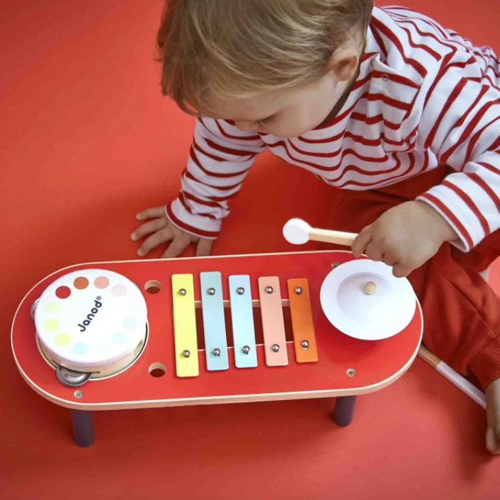 Child playing with a colorful toy drum set on a red floor