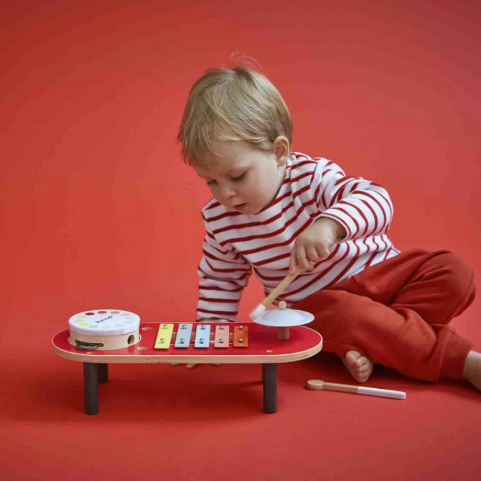 Child playing with a toy xylophone on a red background
