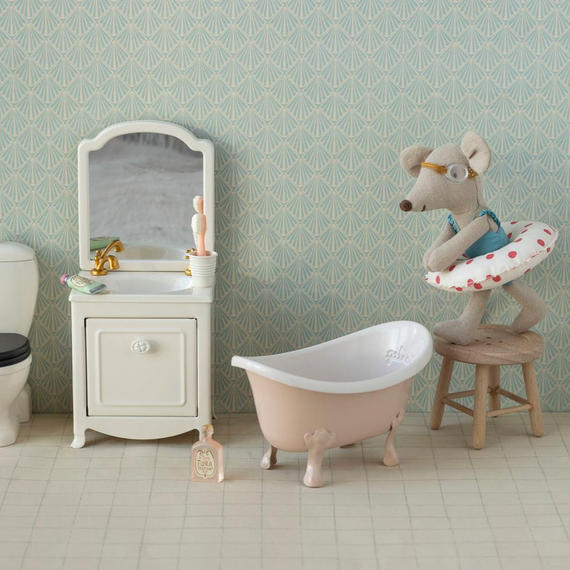 Miniature bathroom set with sink, toilet, bathtub, and decorative elements against a patterned wall.