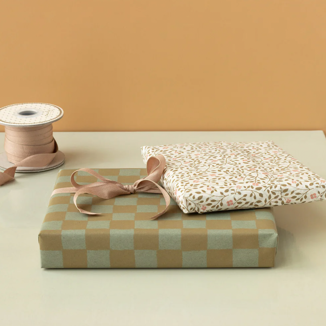 Two wrapped gifts with ribbons on a beige surface against a mustard yellow wall.