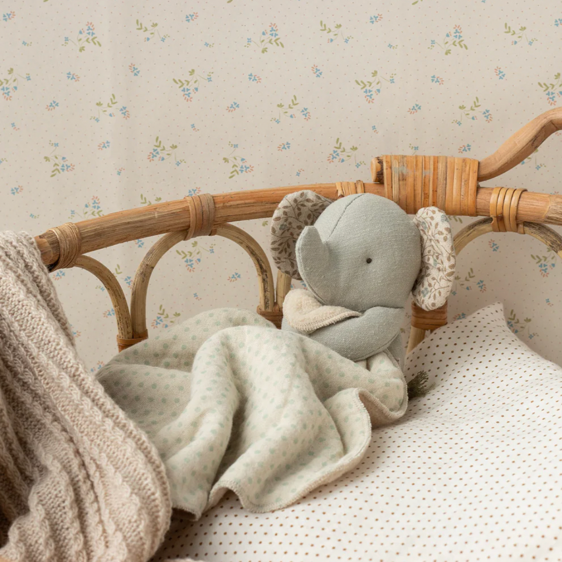 Gray elephant plush toy in a crib with a textured blanket and floral wallpaper.