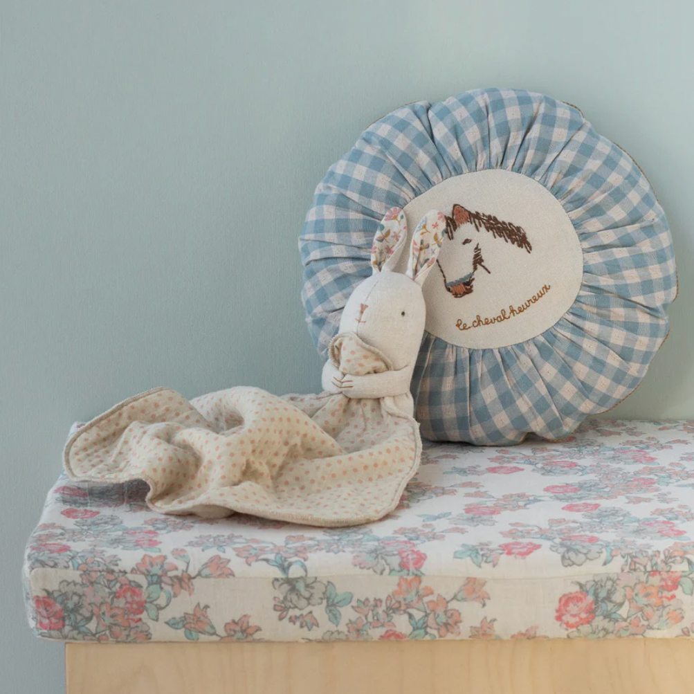 Stuffed animal toy on a floral bed with a decorative pillow against a light blue wall.