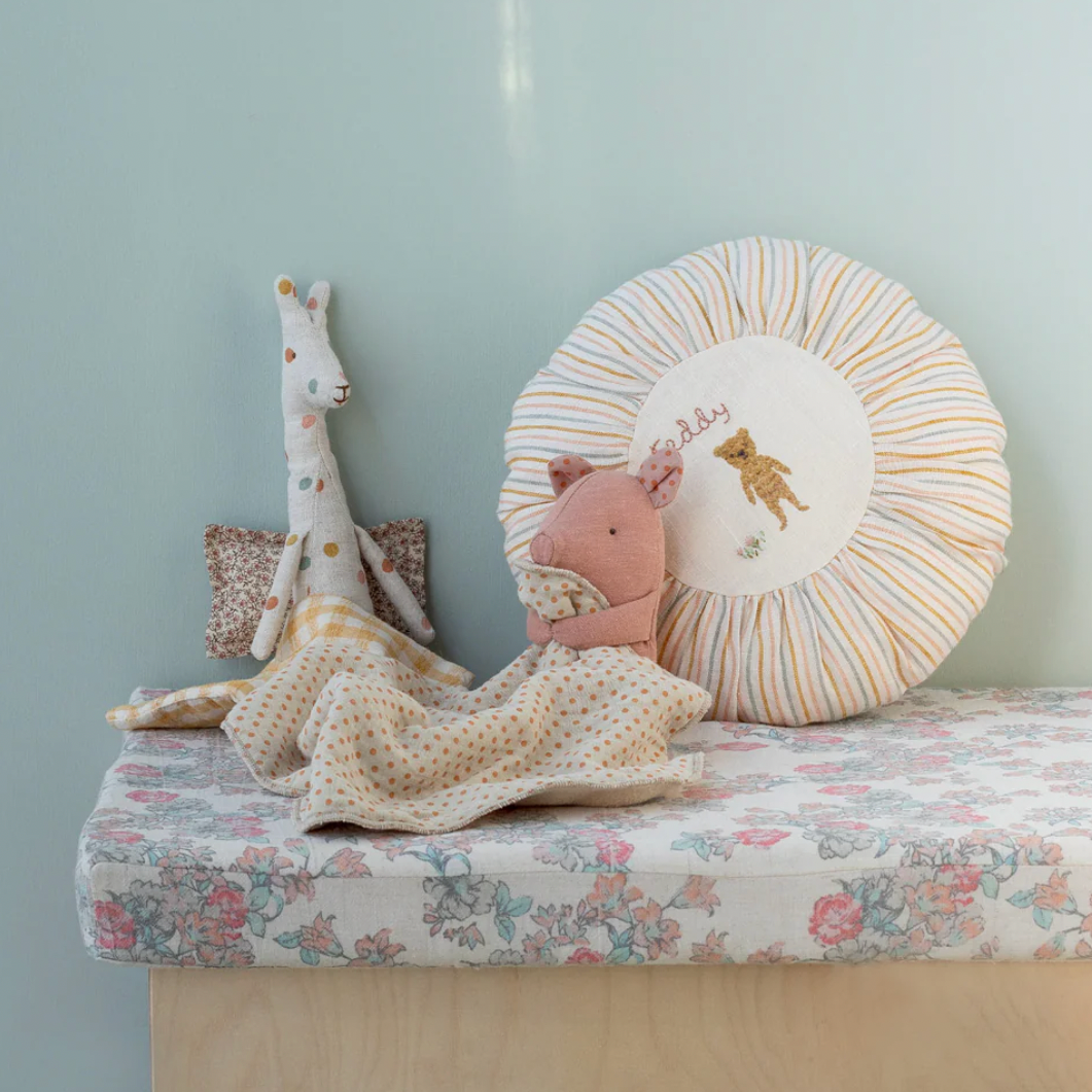 Children's room with a bench, plush toys, and decorative pillows against a light blue wall.