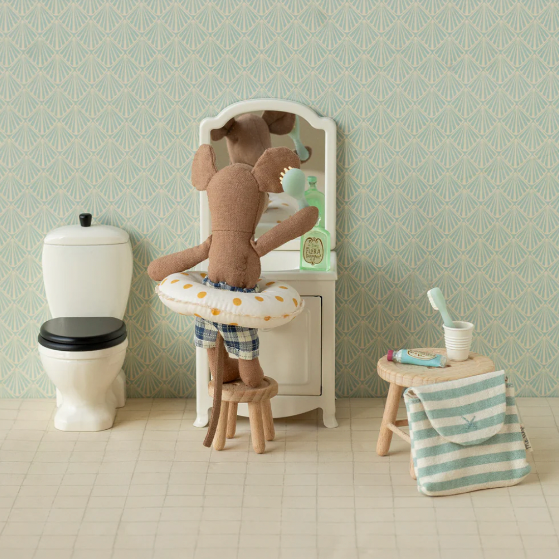 Miniature bathroom set with toy mouse, sink, and toilet against a light green wall.