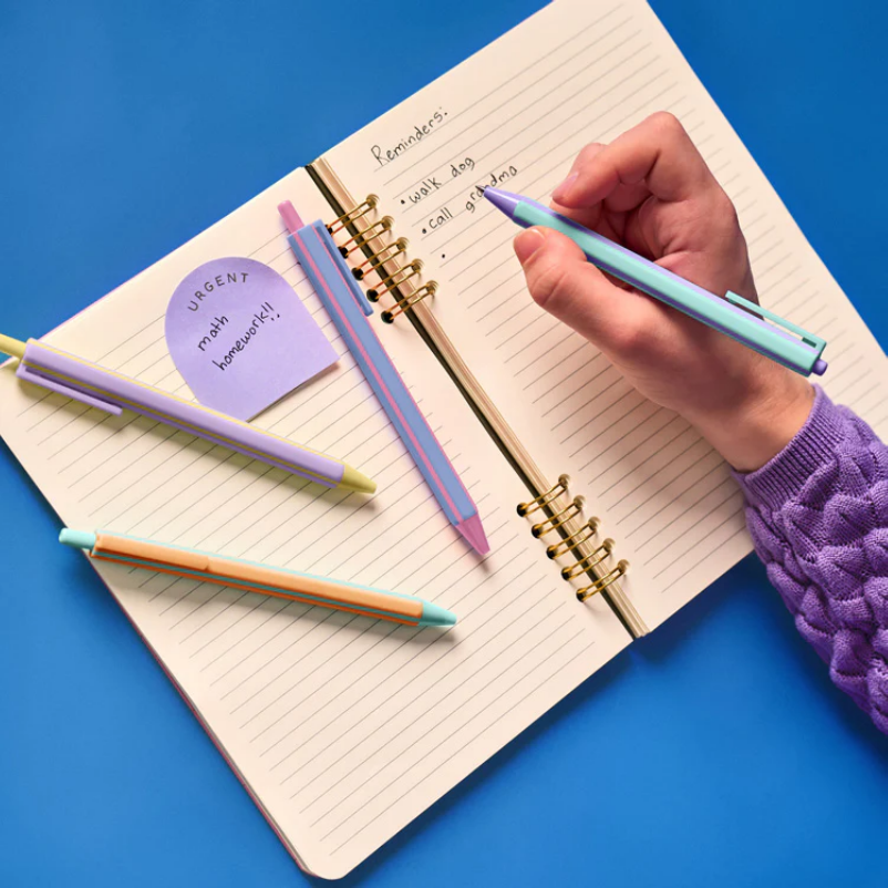 Hand holding a pen over an open planner with colorful pens and sticky notes on a blue background