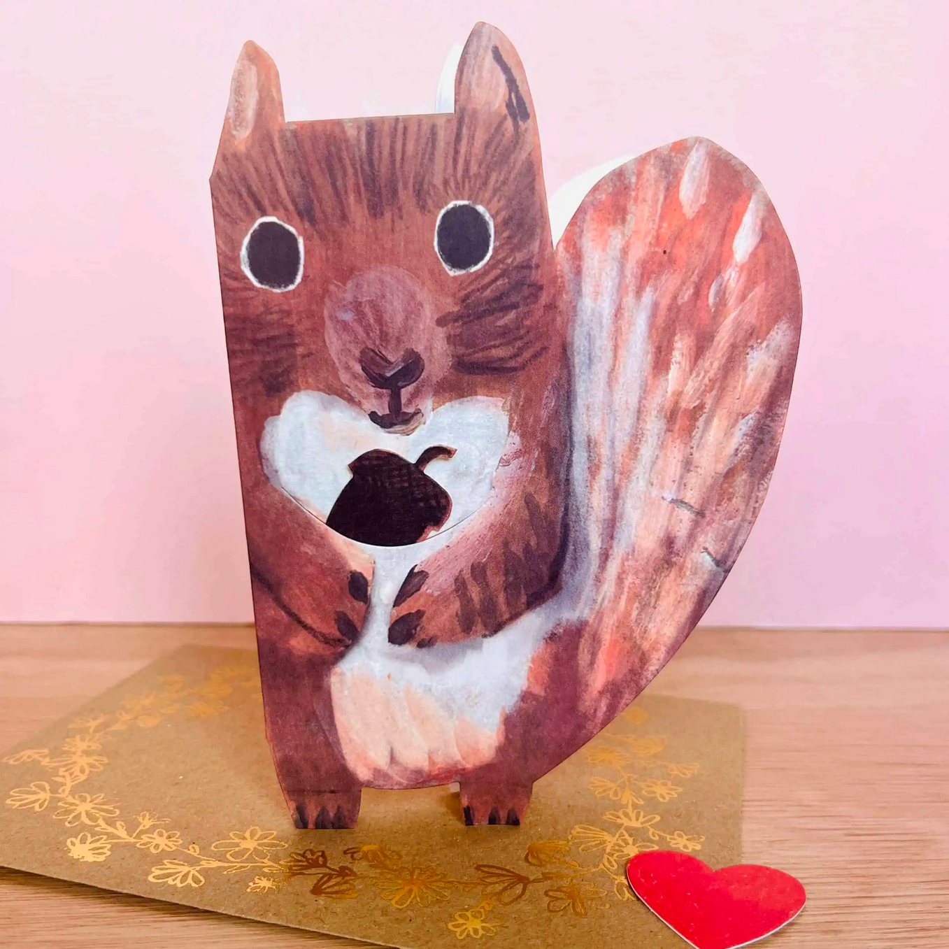 Card with a 3D squirrel design on a wooden surface with a pink background