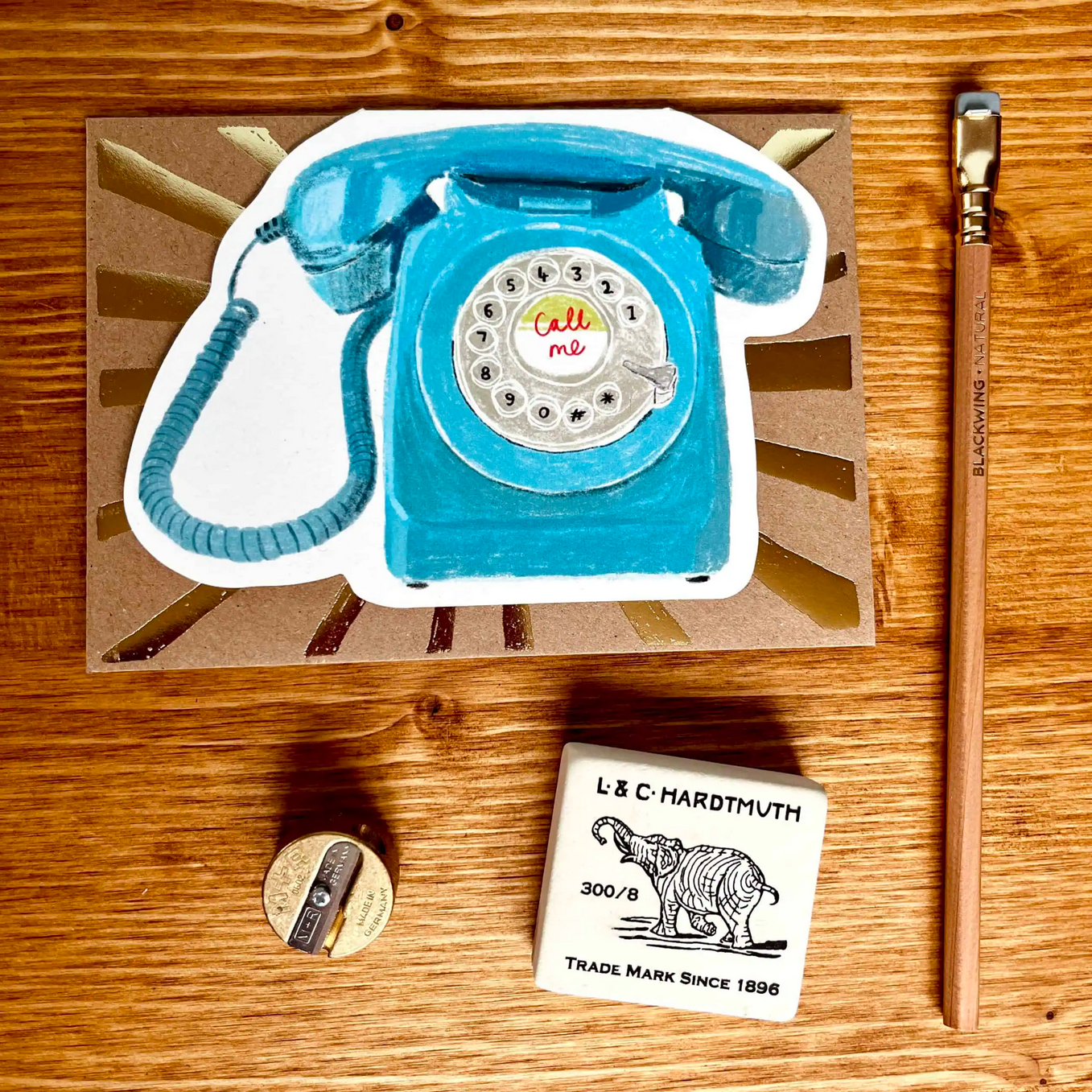 Blue rotary phone card on a wooden surface with a sharpener and stamp visible.