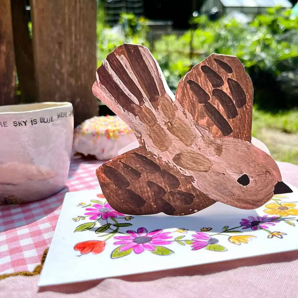 Wooden bird figurine on a floral card with a garden background