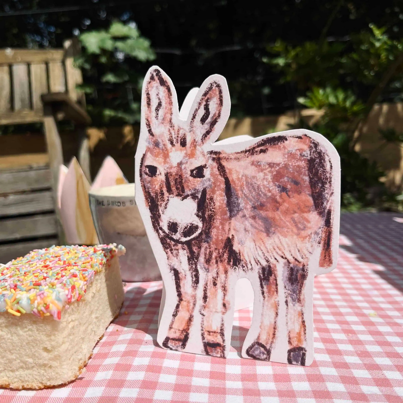Donkey-shaped card on a checkered tablecloth with a cake in the background