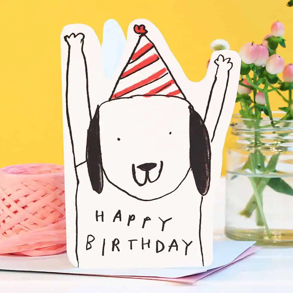Birthday card with a dog wearing a party hat and 'Happy Birthday' text, against a yellow background.