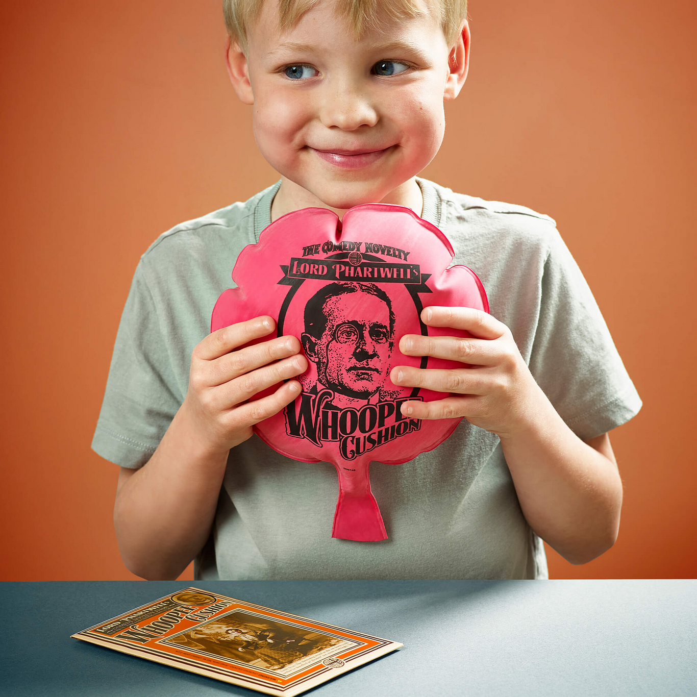 Child holding a pink cushion with a face on it against an orange background