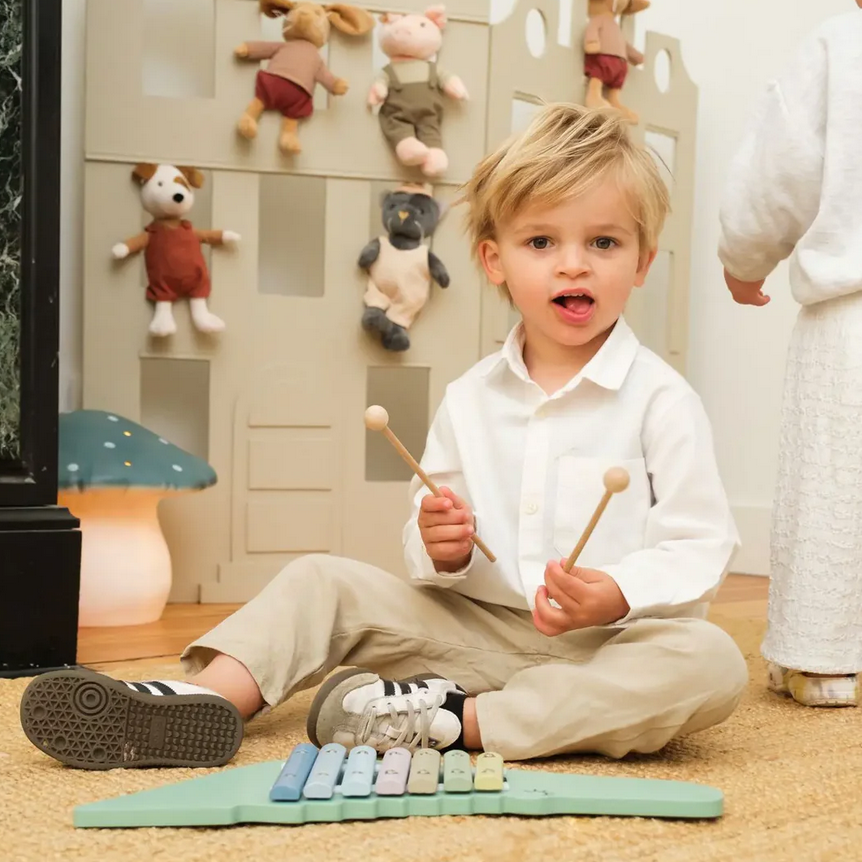 Child playing with musical instruments on the floor in a room with toys hanging on the wall.