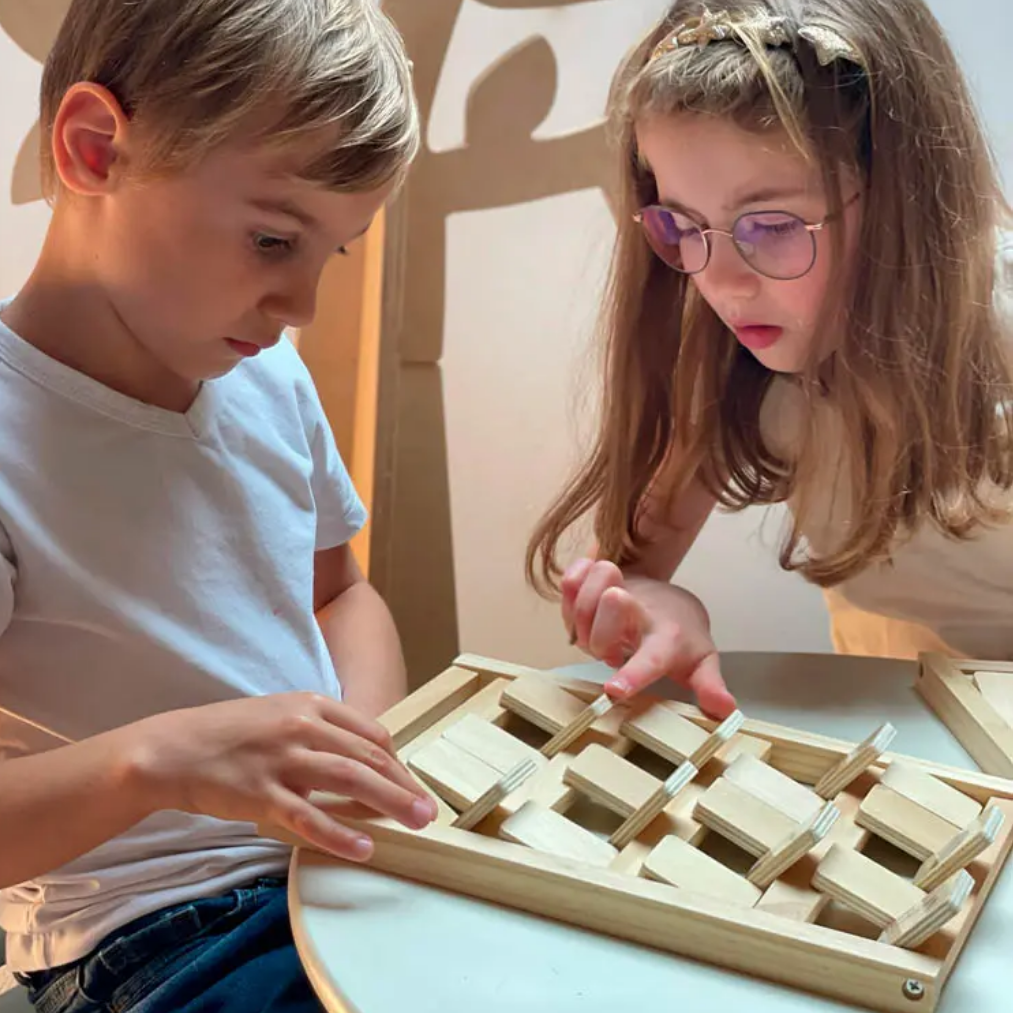 Two children playing with a wooden puzzle at a table.