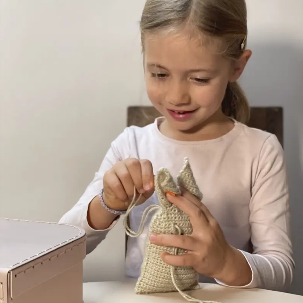 Young girl crafting a small knitted item at a table.