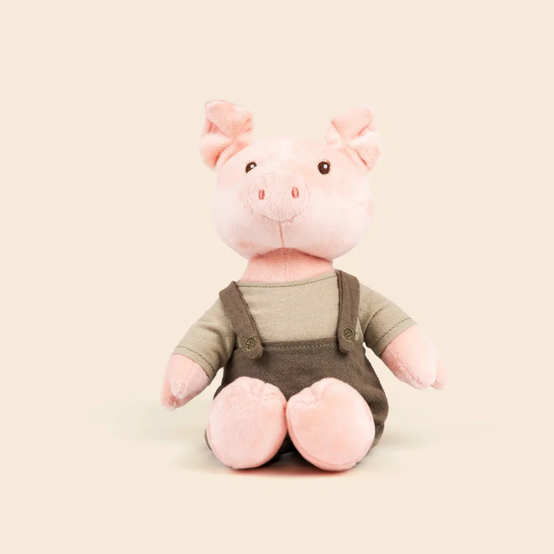 Plush pig toy wearing overalls on a beige background