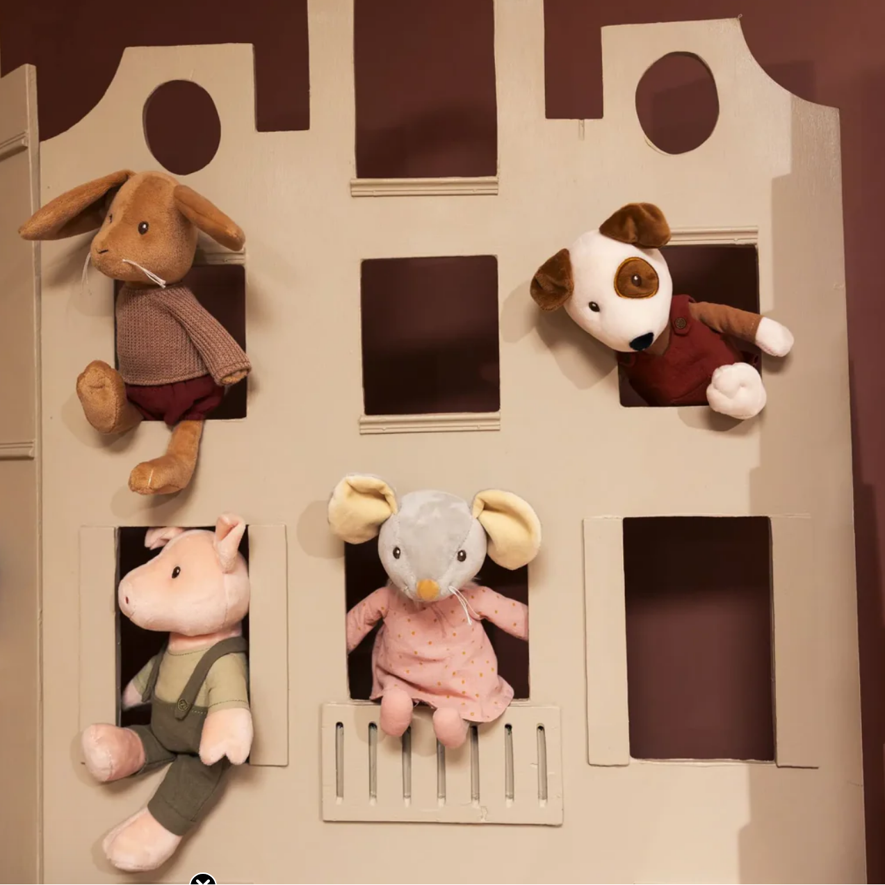 Cardboard playhouse with cut-out windows featuring stuffed animal toys inside.