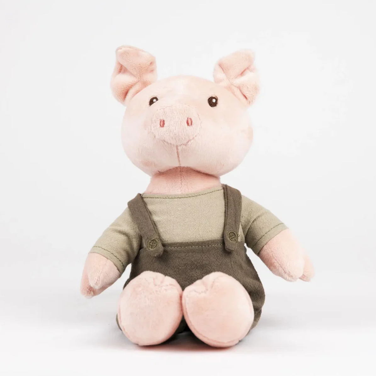 Plush toy pig wearing a green shirt and brown overalls on a white background
