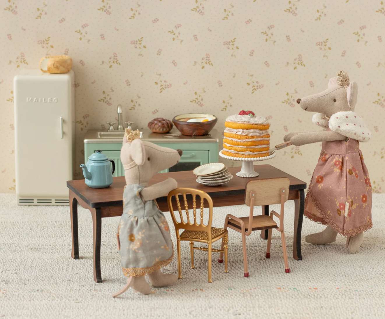 Two toy mice in a kitchen setting with a cake on a table.