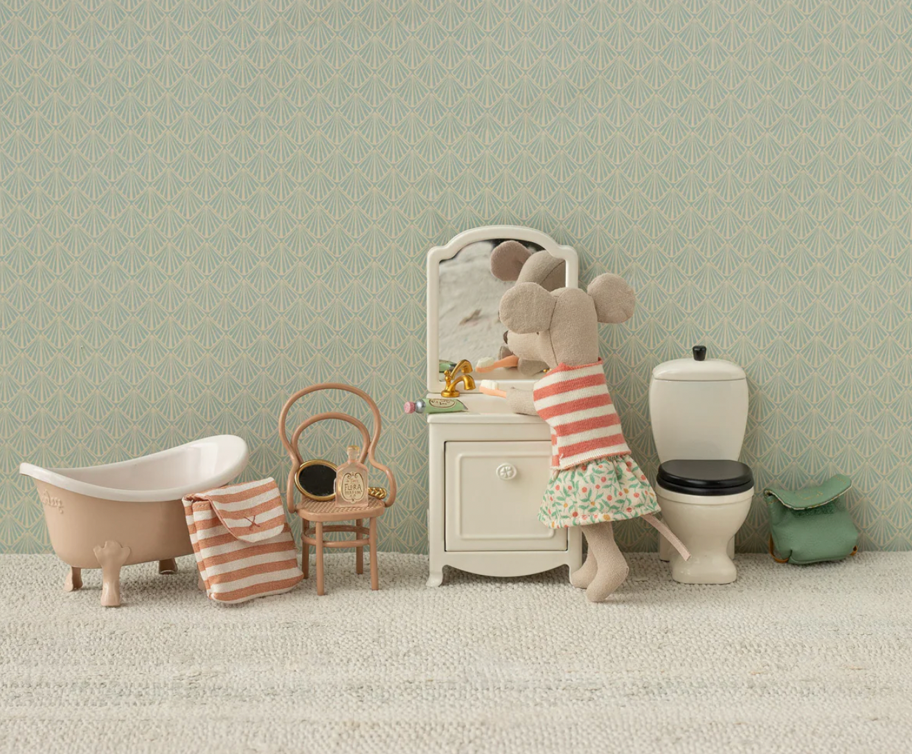Children's bathroom set with toy bathtub, sink, and toilet against a green wall.
