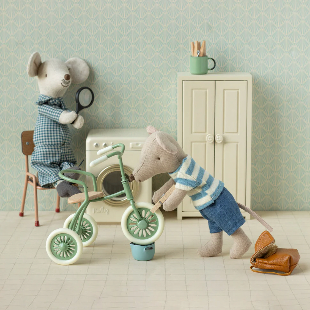 Two toy mice with a tricycle in a room setting, featuring a washing machine and cabinet.