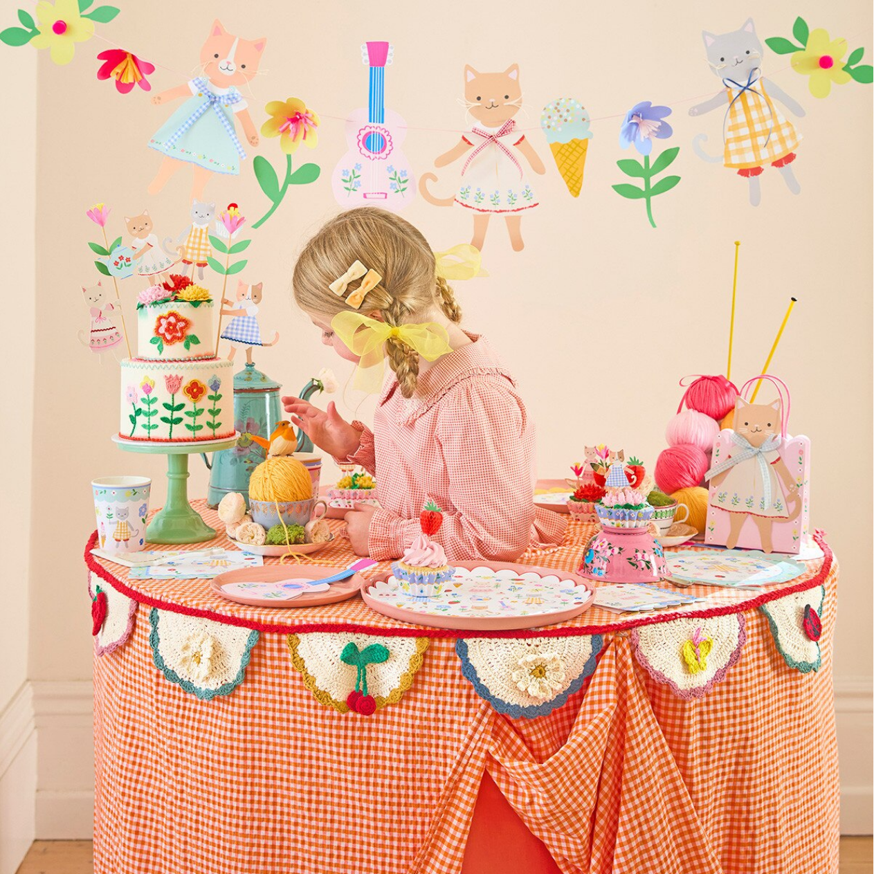 Child playing with a tea party set on a decorated table, surrounded by wall stickers of children and flowers.