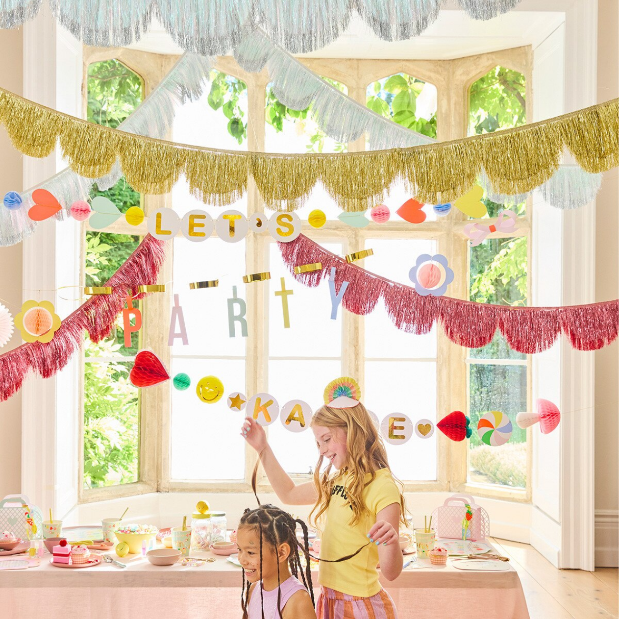 Two children in a room decorated with colorful party banners and decorations.