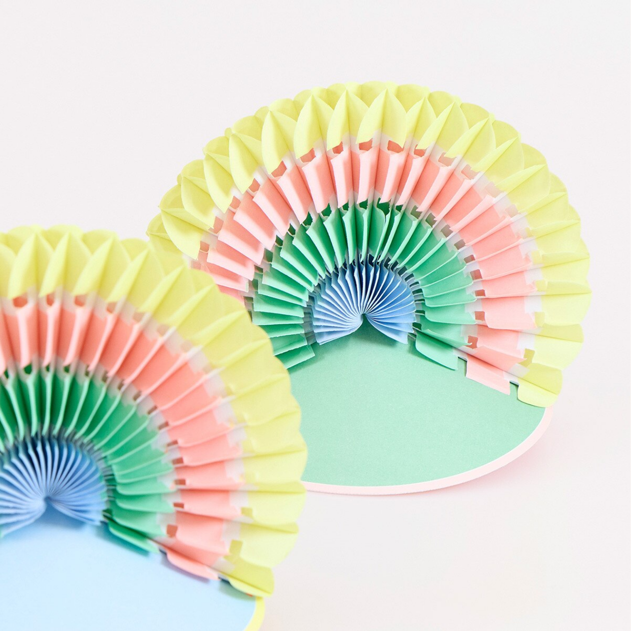 Colorful paper fan hats on a light pink background