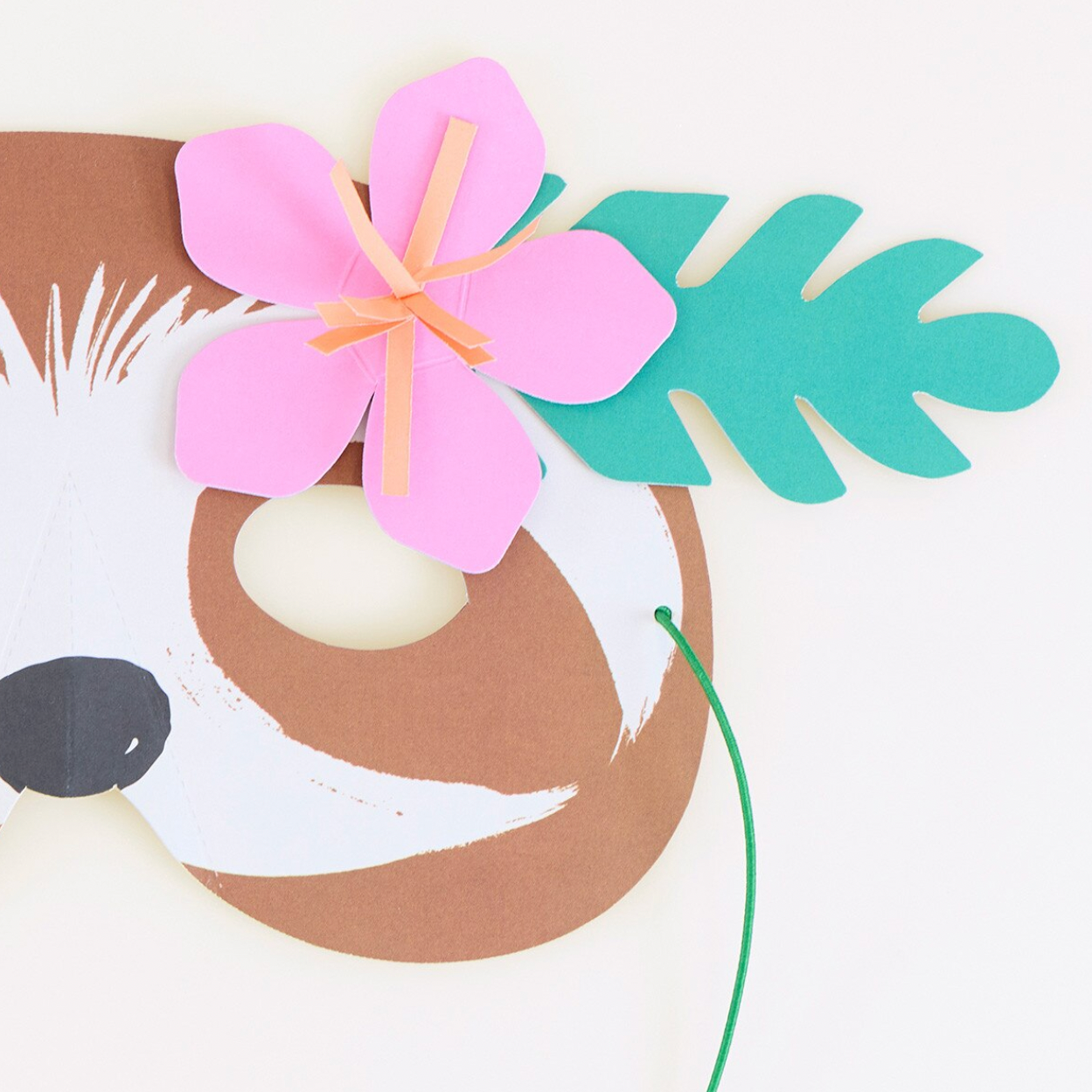Crafted sloth mask with pink flower and green leaves on a white background