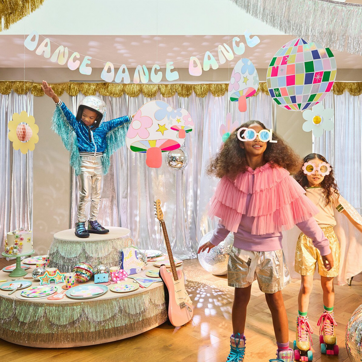 Children in colorful costumes at a party with decorations and a 'Dance Dance Dance' banner.