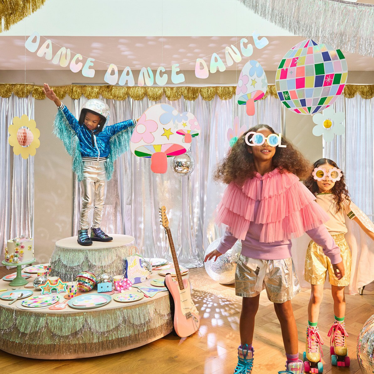 Children in colorful costumes at a party with decorations and a 'Dance Dance Dance' banner.