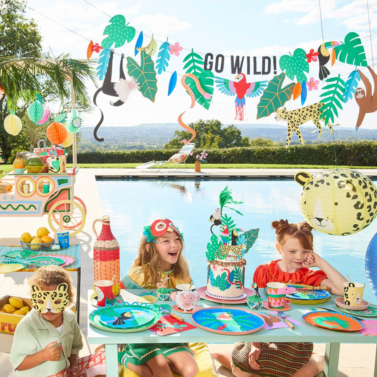 Children's birthday party with jungle-themed decorations and cake by a pool.