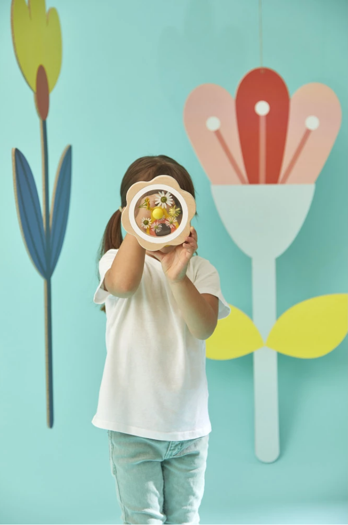 Child holding a plate with colorful flowers in front of a floral-themed wall.